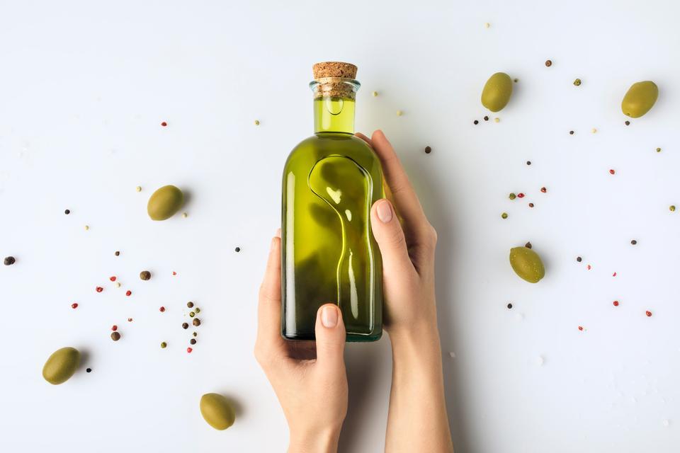 Cropped image of woman holding glass bottle of olive oil in hands isolated on white